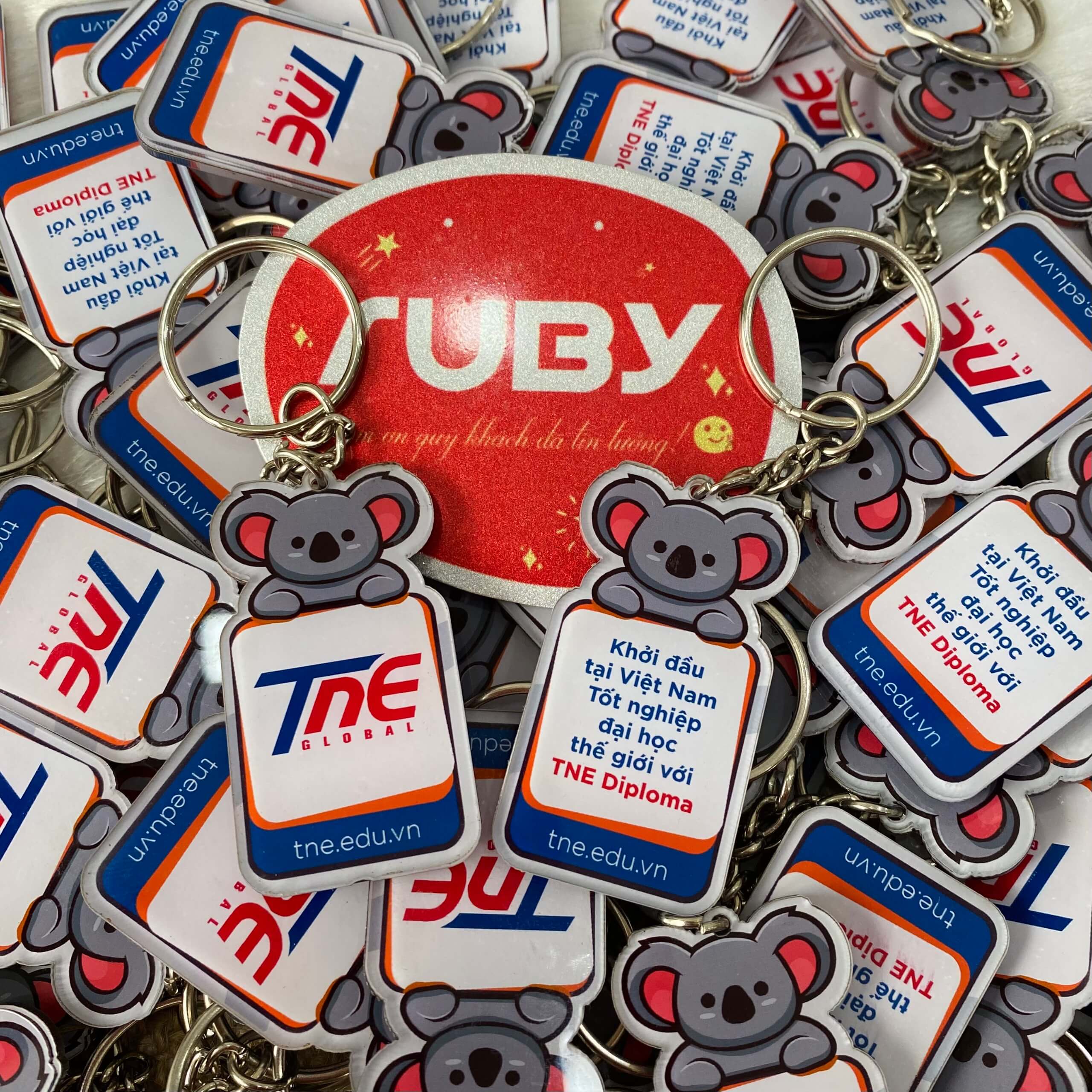 Móc khóa in logo TNE Global hình chú gấu Koala cầm bảng thông điệp, thiết kế hai mặt sắc nét, chất liệu mica Đài Loan