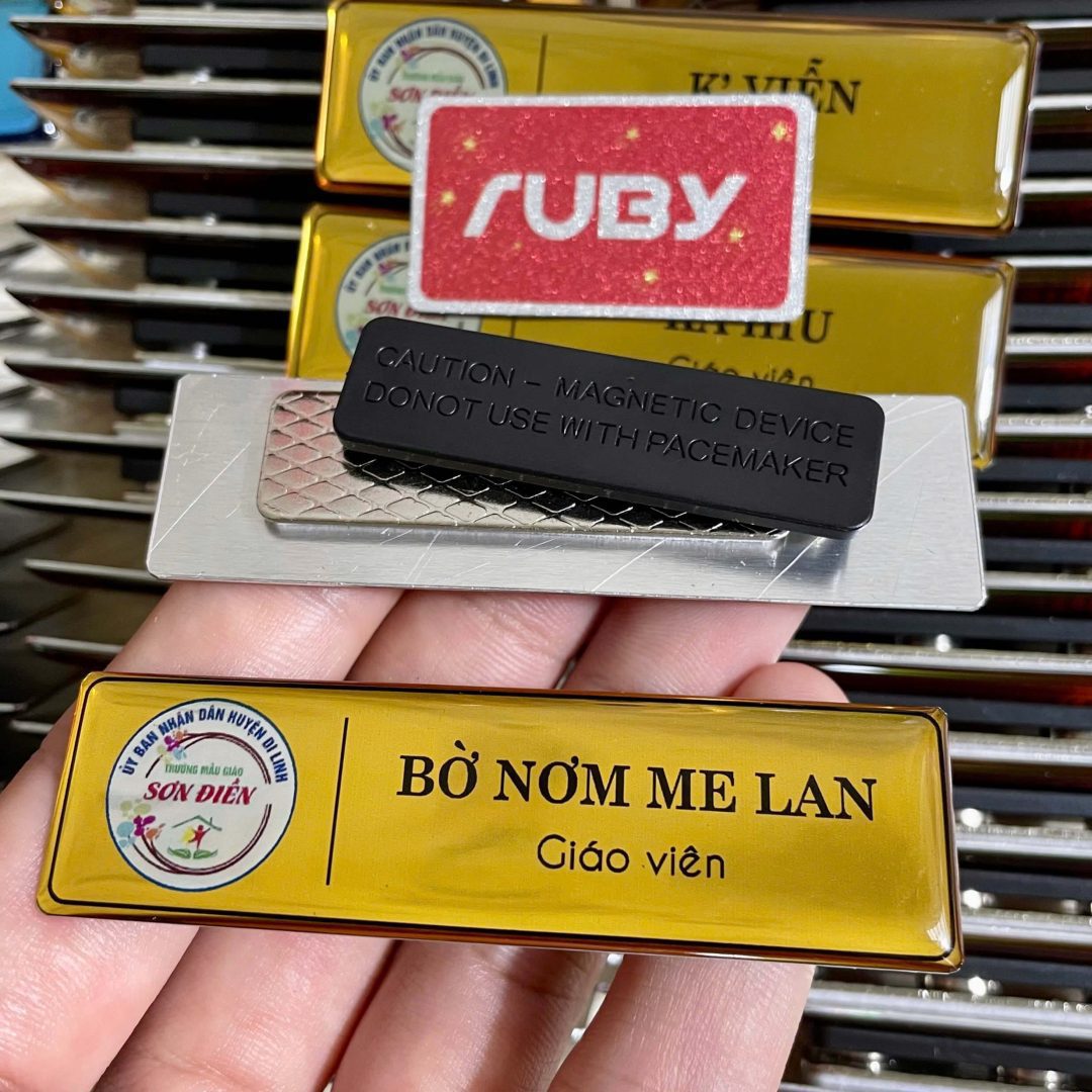 Bảng tên giáo viên nam châm bằng nhôm nền vàng của Trường Mẫu giáo Sơn Điền, in tên “Bờ Nơm Me Lan”; mặt sau nam châm 3 nút, không thủng áo.
