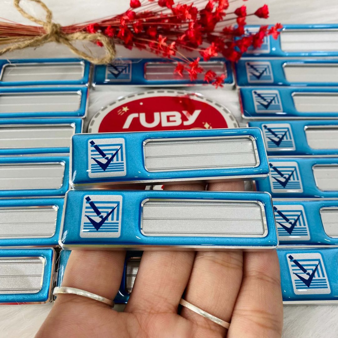 Bảng tên nhân viên nền xanh bằng nhôm, có logo tick xanh, phần giữa trượt thay tên được.
