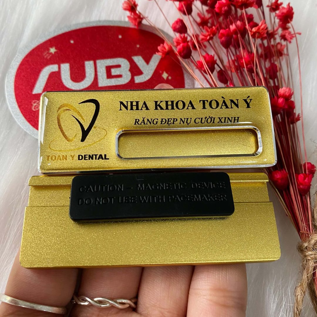 Bảng tên nhân viên Nha Khoa Toàn Ý, nền vàng, in logo và slogan “Răng đẹp nụ cười xinh”, gắn nam châm.
