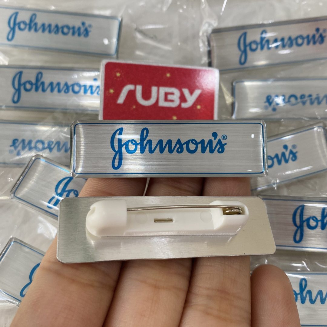 Huy hiệu nhôm in logo Johnson’s nền bạc xước cao cấp, in logo màu xanh, phủ keo trong bóng đẹp