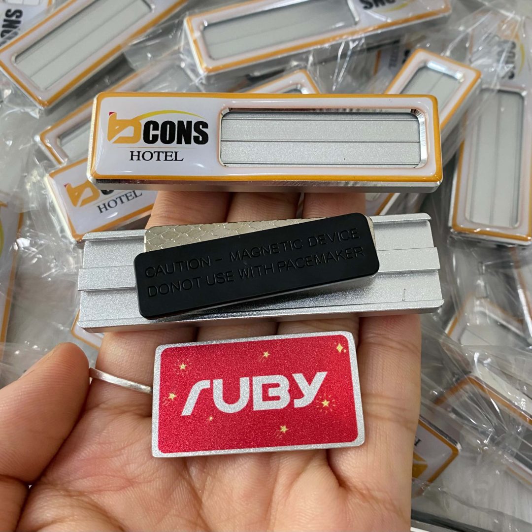 Bảng tên nhân viên khách sạn BCons Hotel nền bạc viền cam, logo chữ B màu vàng, gắn nam châm.