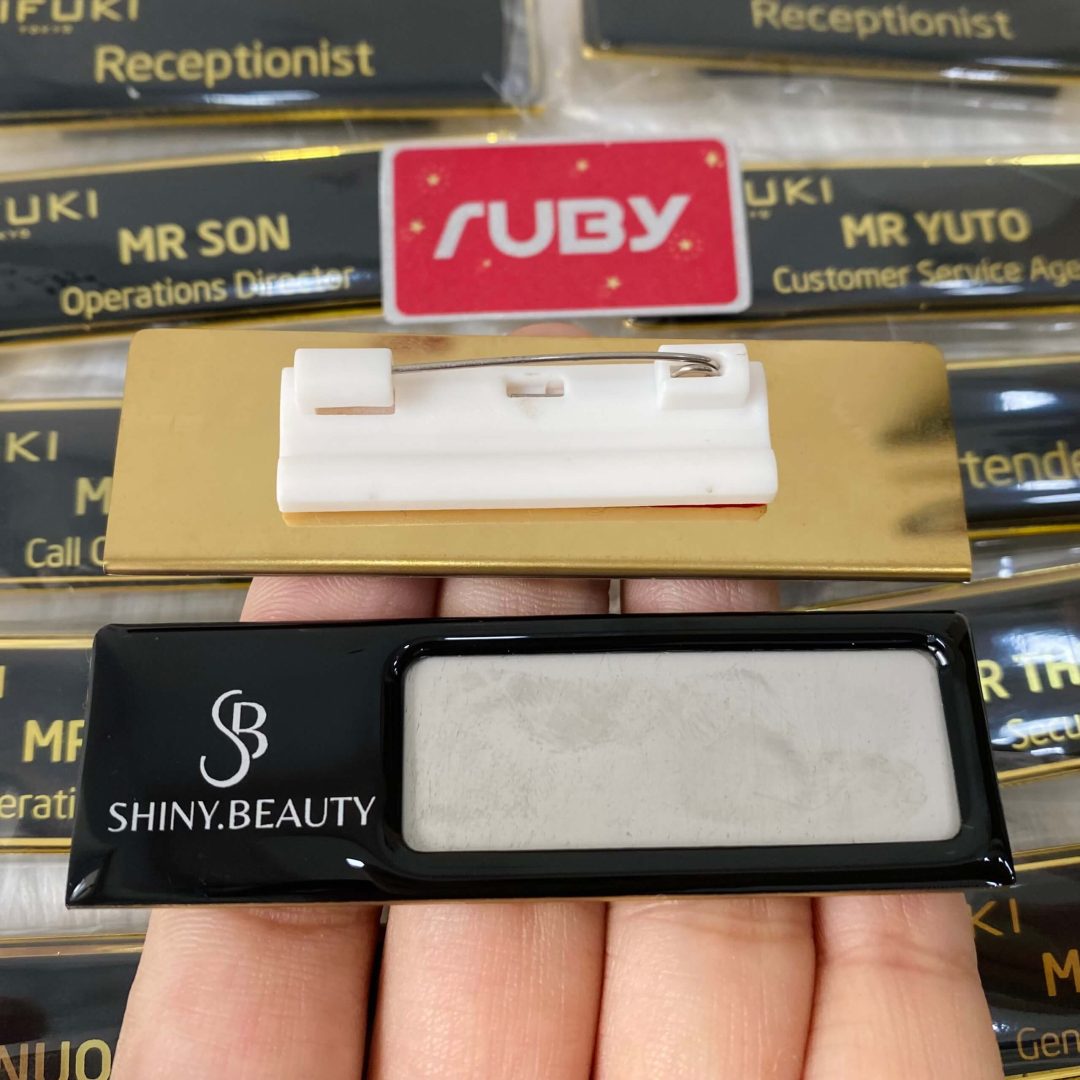 Bảng tên Shiny Beauty inox đen phủ bóng, logo trắng, gài nhựa.