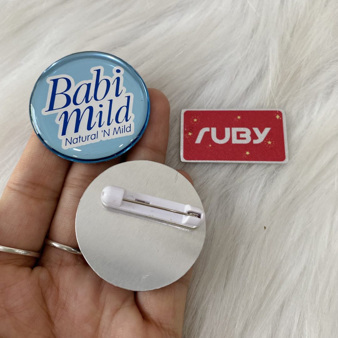 Huy hiệu tròn Babi Mild phủ keo trong, nền xanh dương nhẹ, in logo thương hiệu
