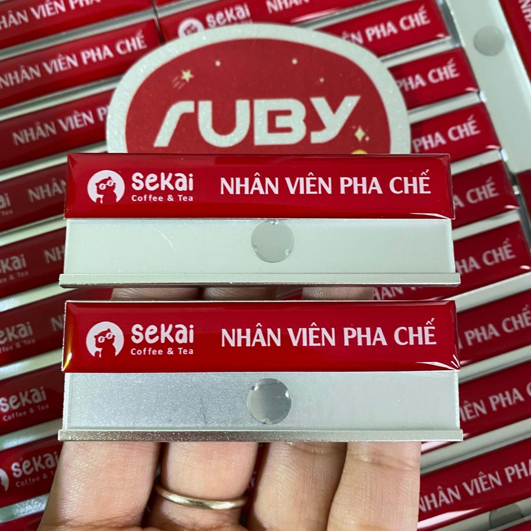 Bảng tên nhân viên pha chế Sekai Coffee & Tea, nền đỏ nổi bật, in logo sắc nét.