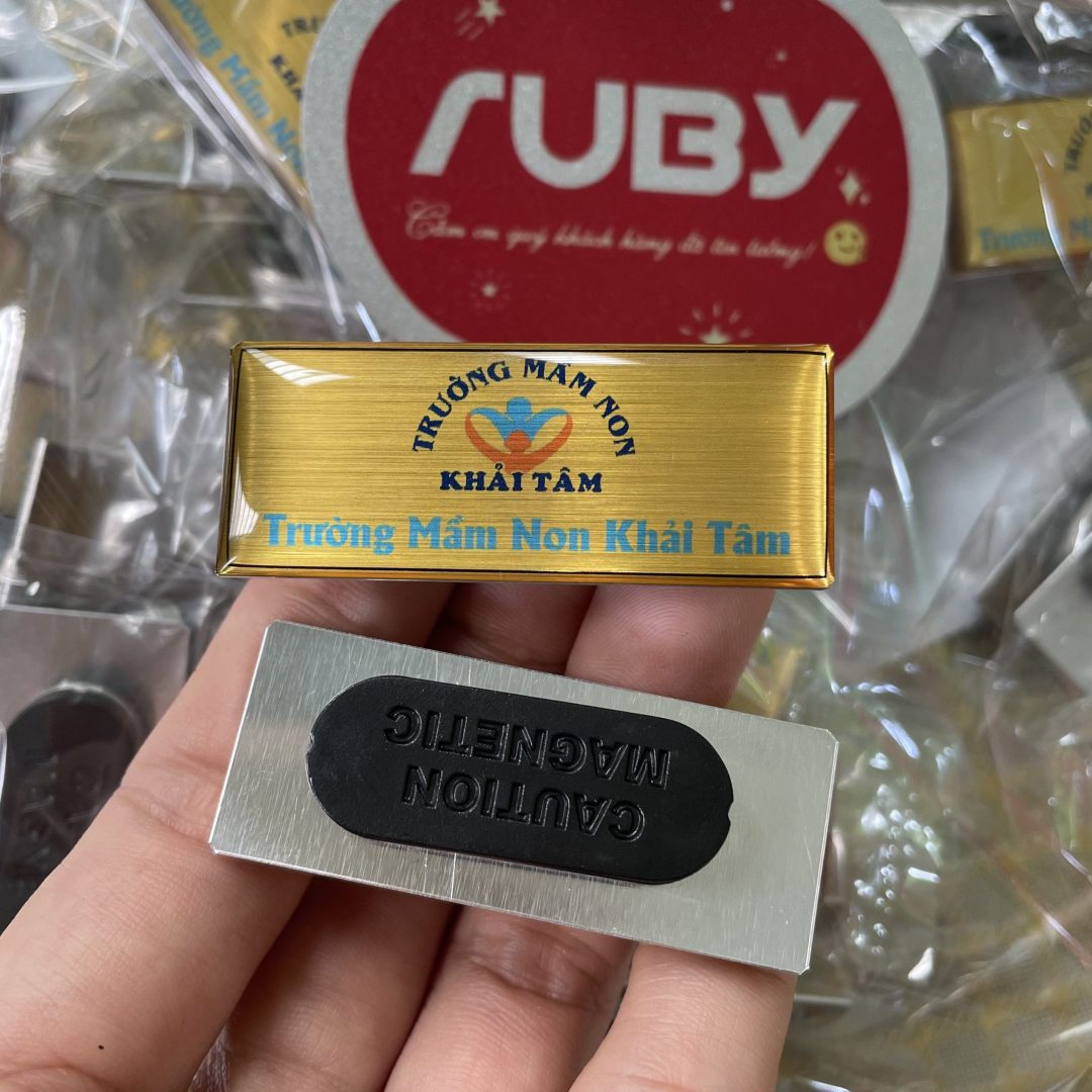 Huy hiệu đeo áo hình chữ nhật in logo Trường Mầm Non Khải Tâm nền vàng xước, in logo, gắn hít nam châm