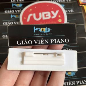Bảng tên giáo viên Piano HaMiLa màu đen, in logo trung tâm âm nhạc, chữ trắng nổi bật, ghim cài áo.