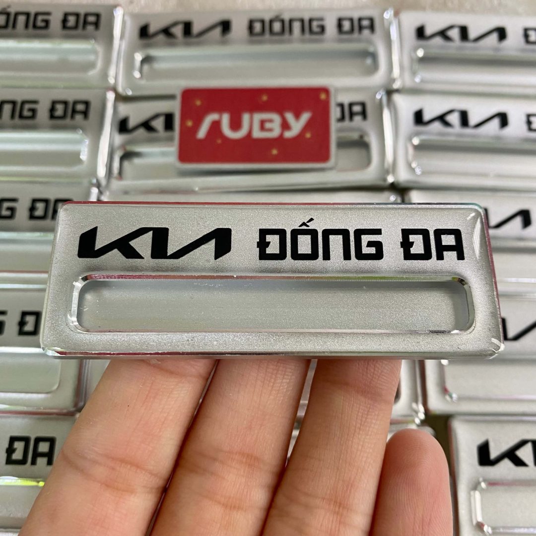 Bảng tên nhân viên KIA Đống Đa, nền bạc, in logo KIA đen hiện đại.