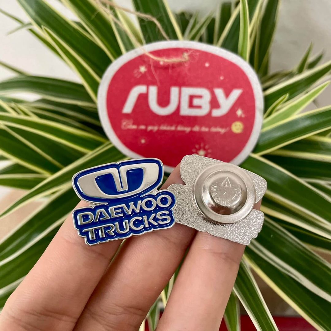Huy hiệu DAEWOO TRUCKS in logo xanh dương, mặt sau chốt gài tròn, bề mặt bạc nhám tinh tế