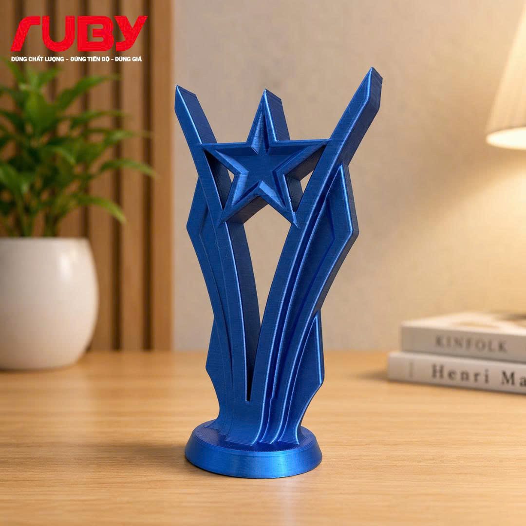 Cận cảnh cúp vinh danh hình ngôi sao 5 cánh in 3D với màu xanh metallic (metallic blue) bóng bẩy, thiết kế tùy chỉnh theo yêu cầu, thương hiệu Ruby. Hình ảnh thể hiện rõ khả năng đổi màu sắc cho phần thân và ngôi sao. Đặt trên bàn gỗ trong không gian văn phòng.